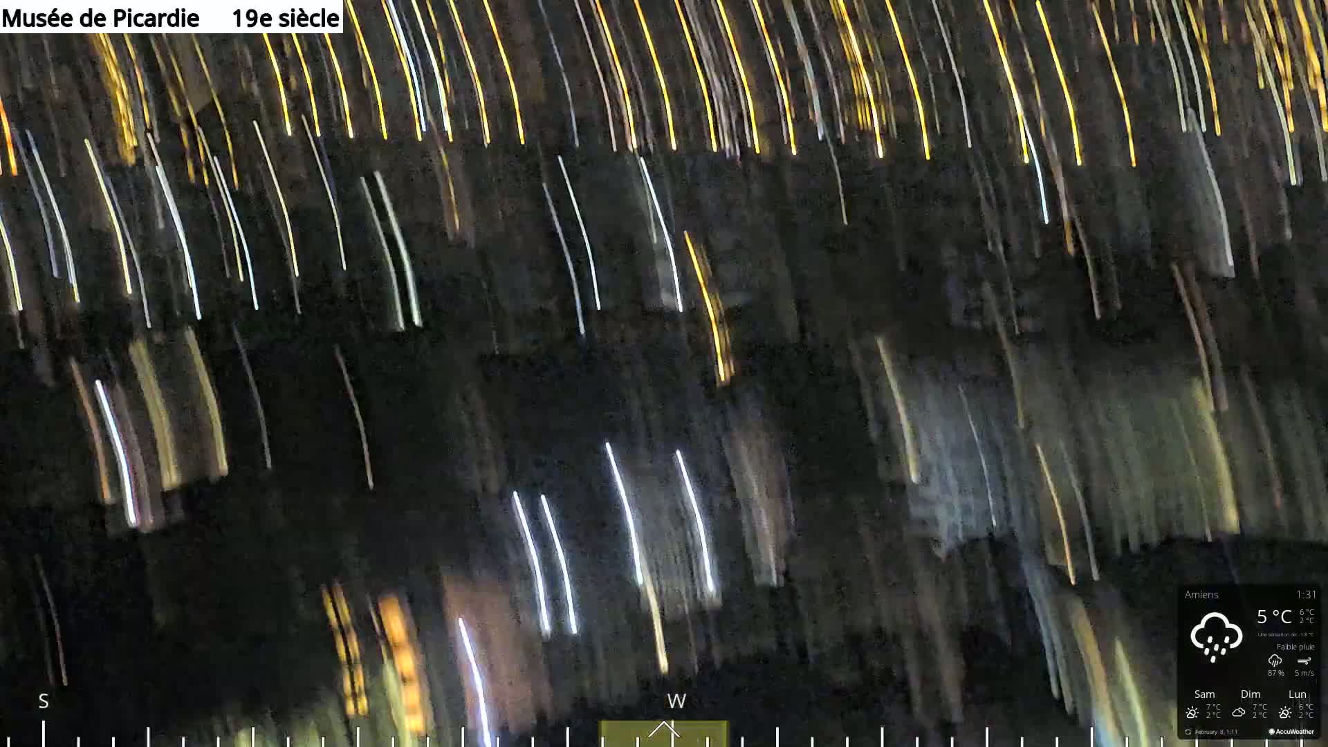 A long-exposure nighttime image shows streaks of light moving diagonally across a dark background under light rain.