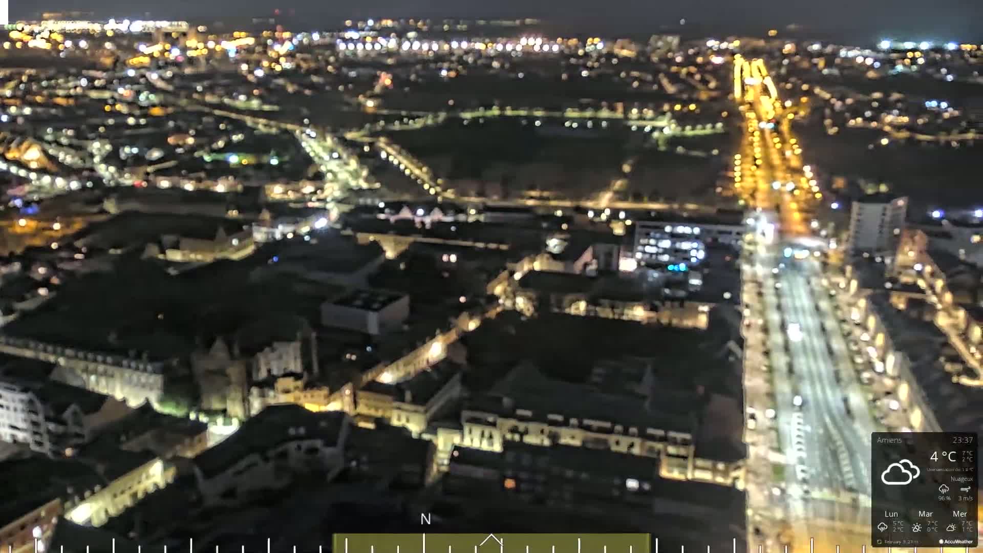 A nighttime aerial view of a city with brightly lit streets and buildings under cloudy skies.