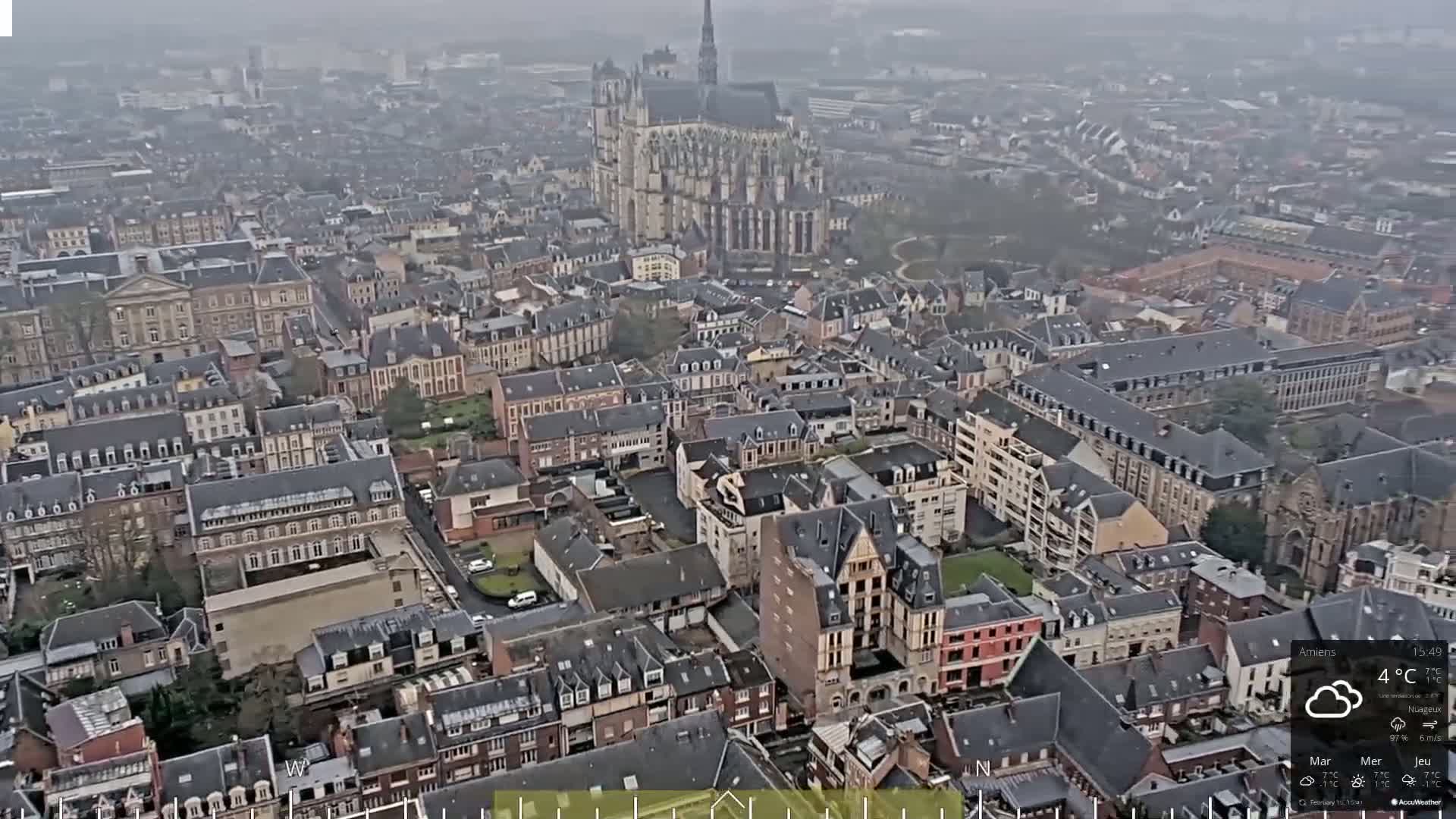 A high-angle, long shot of a city on an overcast day, showcasing a large cathedral in the background and numerous buildings of varying heights and architectural styles.