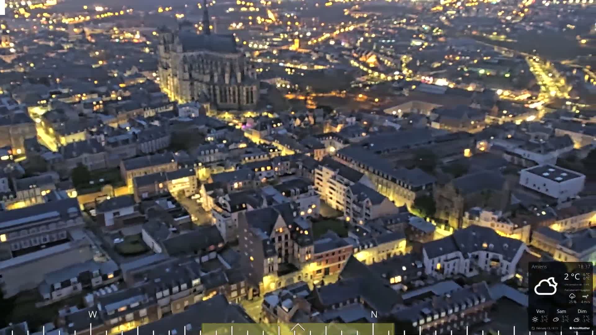 An aerial nighttime view of a European city with illuminated buildings and streets under a cloudy sky.