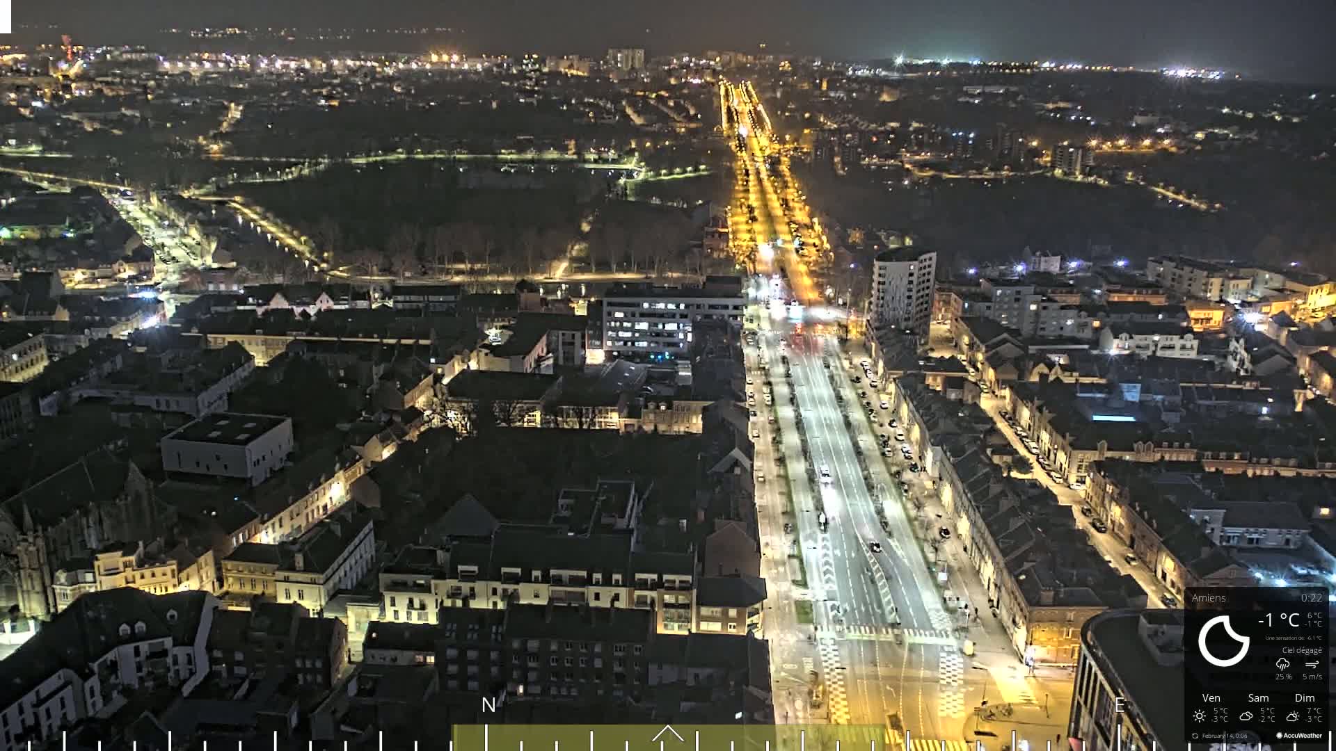 A nighttime, high-angle view of a city with a long, brightly lit street running through its center, under a clear sky.