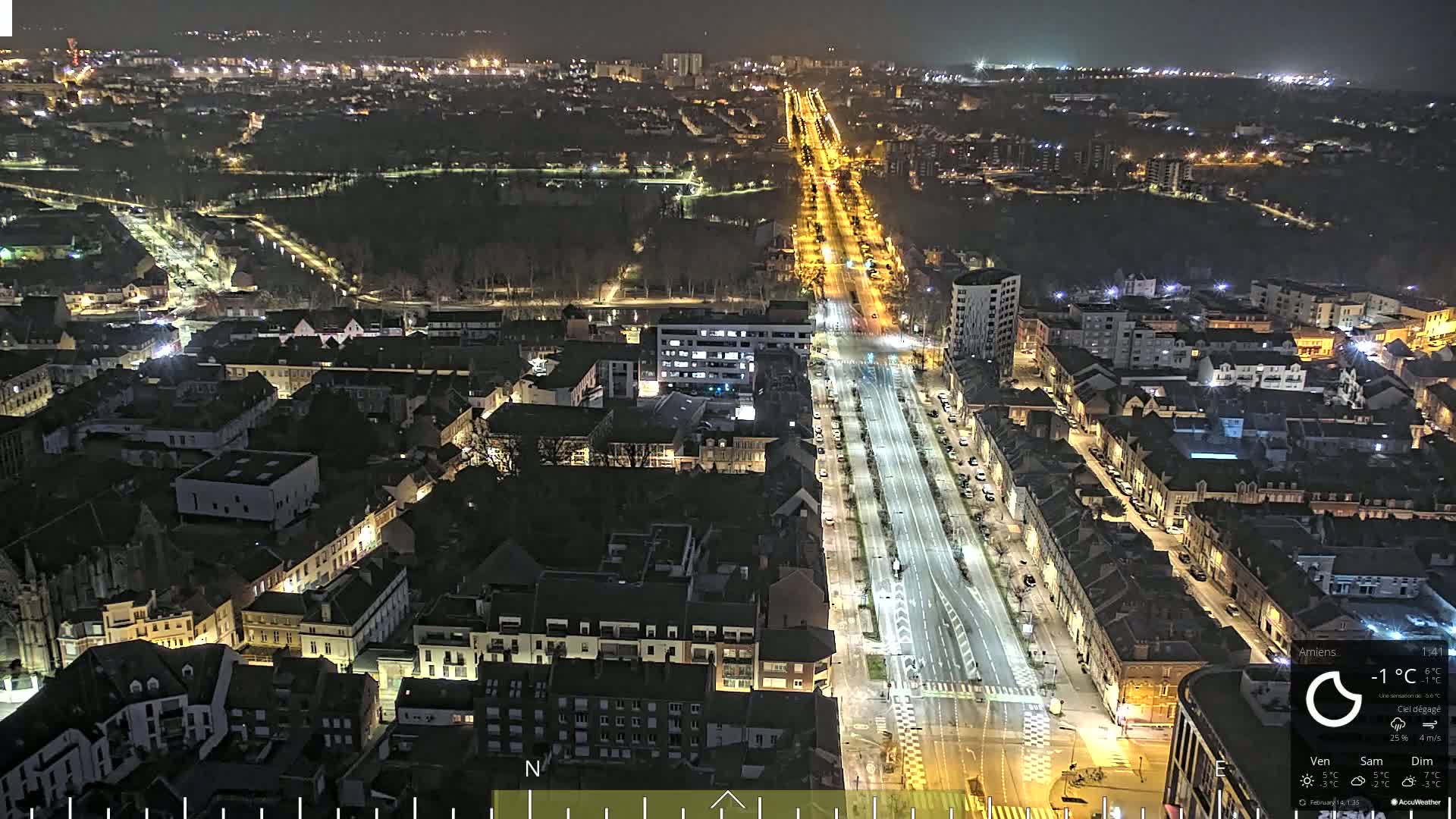 A nighttime aerial view of a city with a long, brightly lit road running through it, under clear skies.