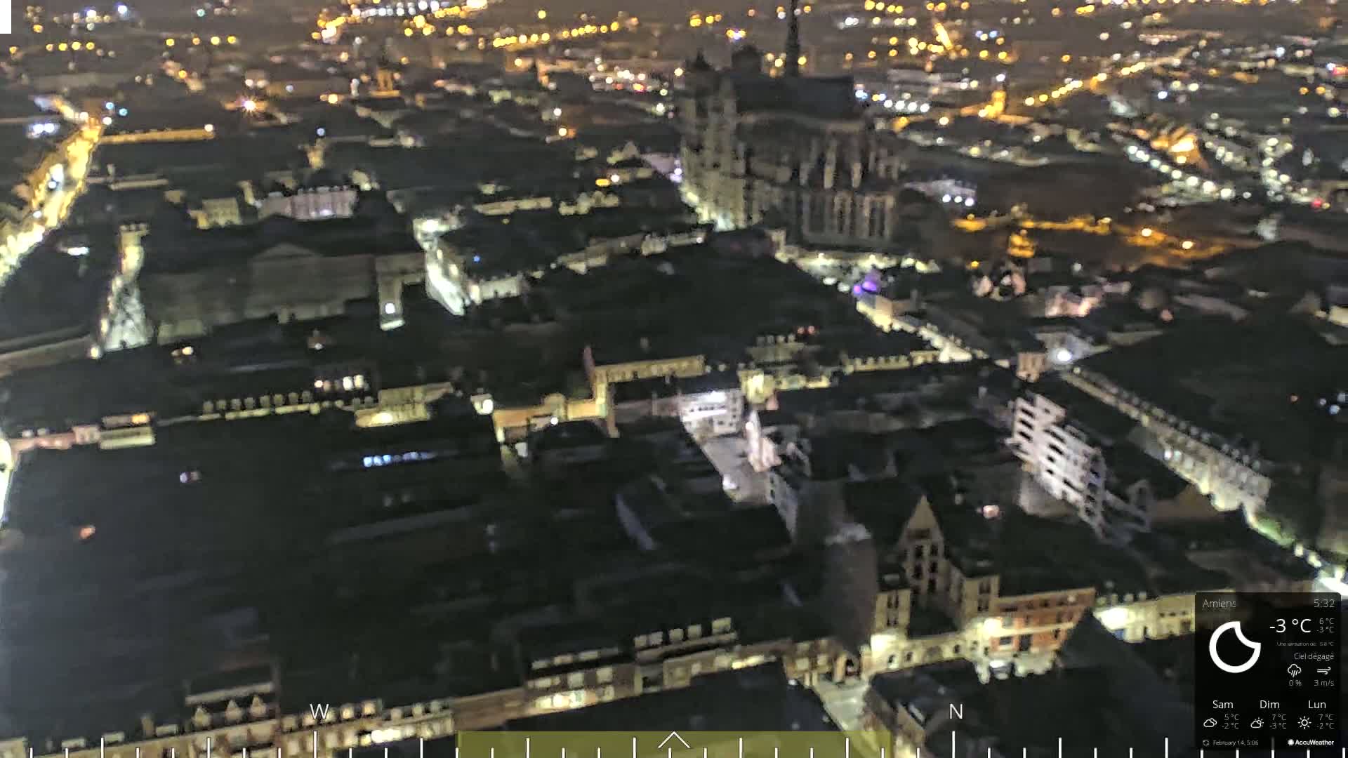 A nighttime aerial view of a city with many illuminated buildings and a large cathedral, under clear skies.