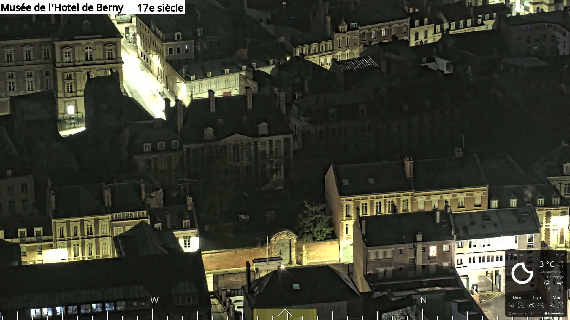 A nighttime aerial view of a European city, showing a collection of closely packed buildings illuminated by streetlights under a clear sky.