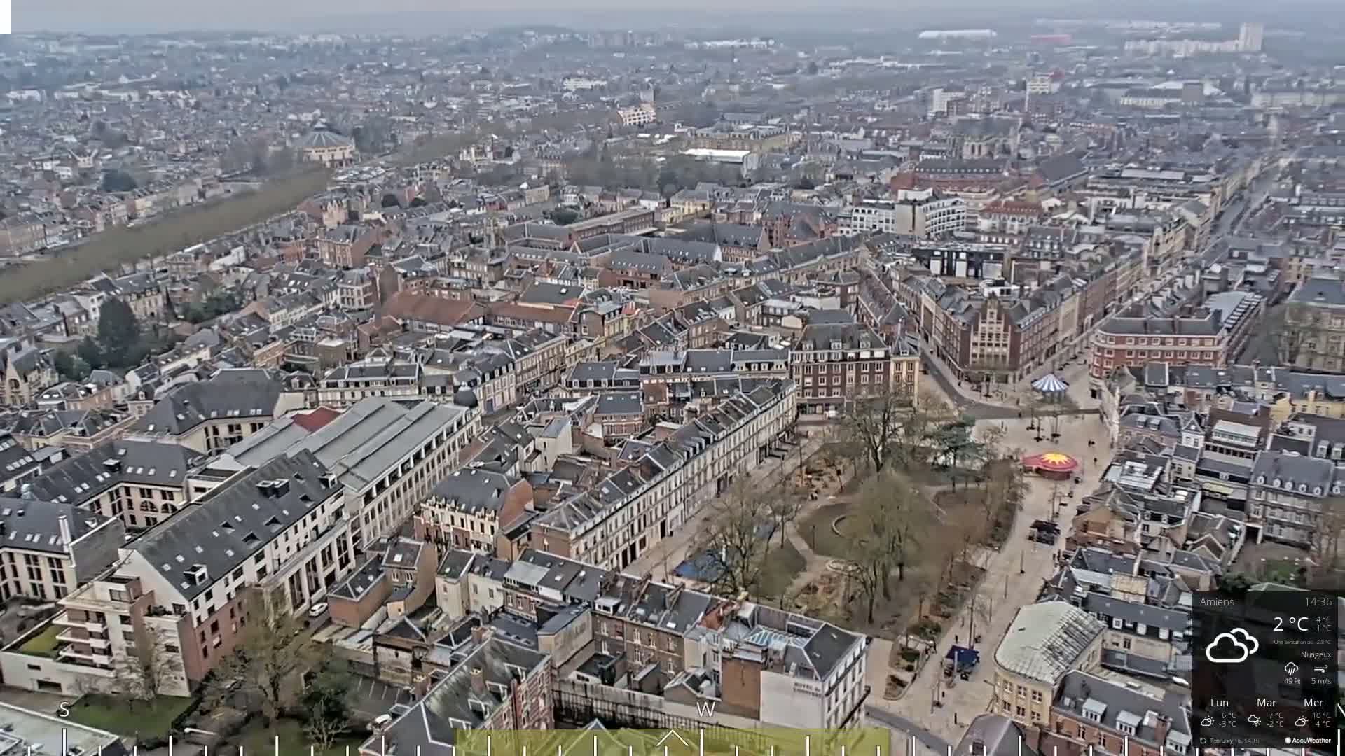 An aerial view of a European city on an overcast day, showing a dense collection of buildings with a central park and a small fairground.