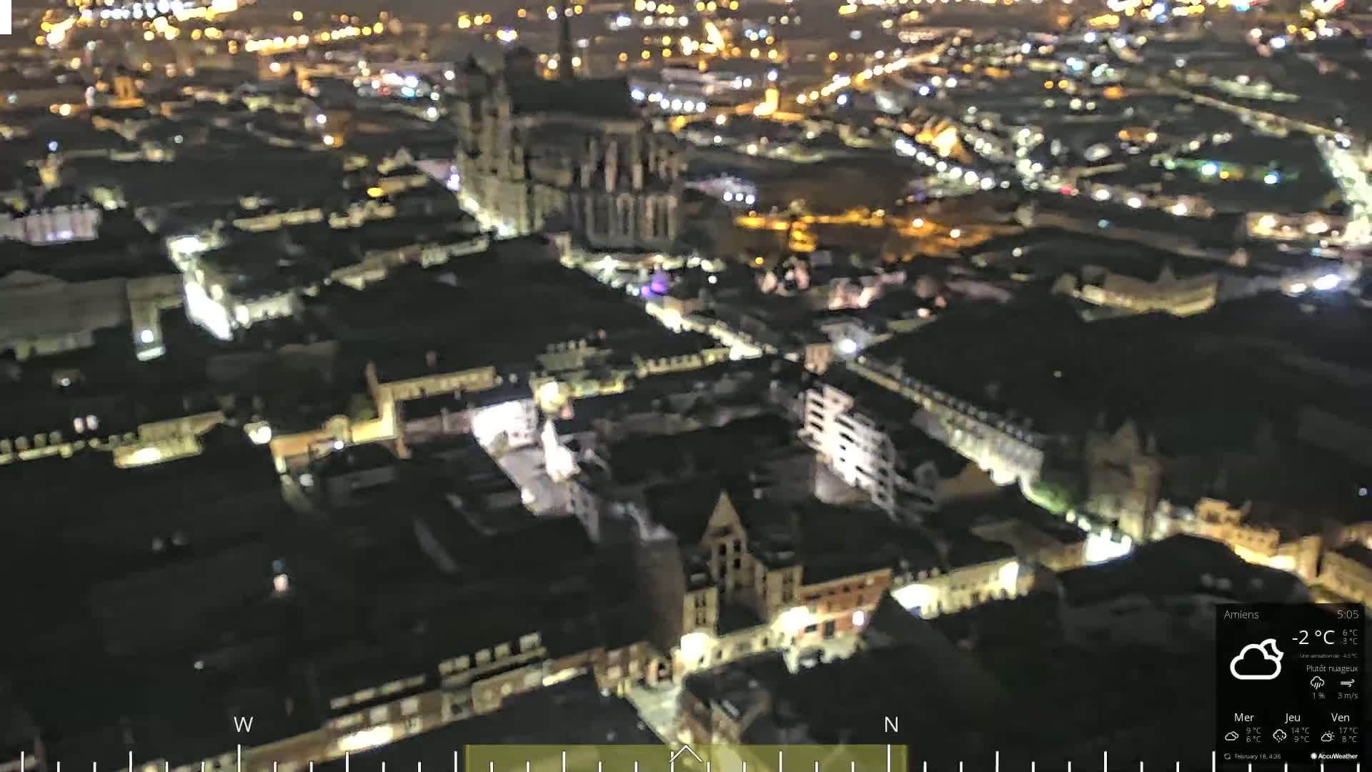 A nighttime aerial view of a city with many illuminated buildings, under partly cloudy conditions.