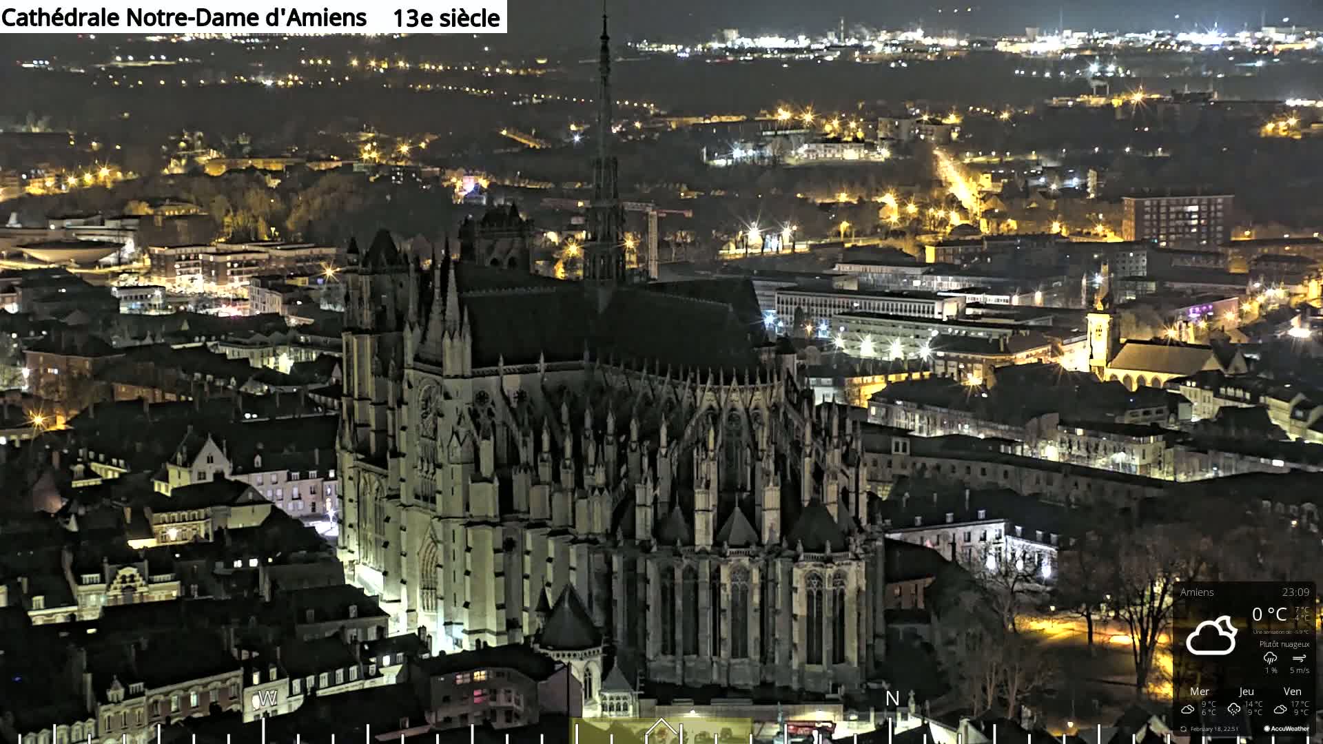A large Gothic cathedral is illuminated at night, surrounded by a city with many lights.