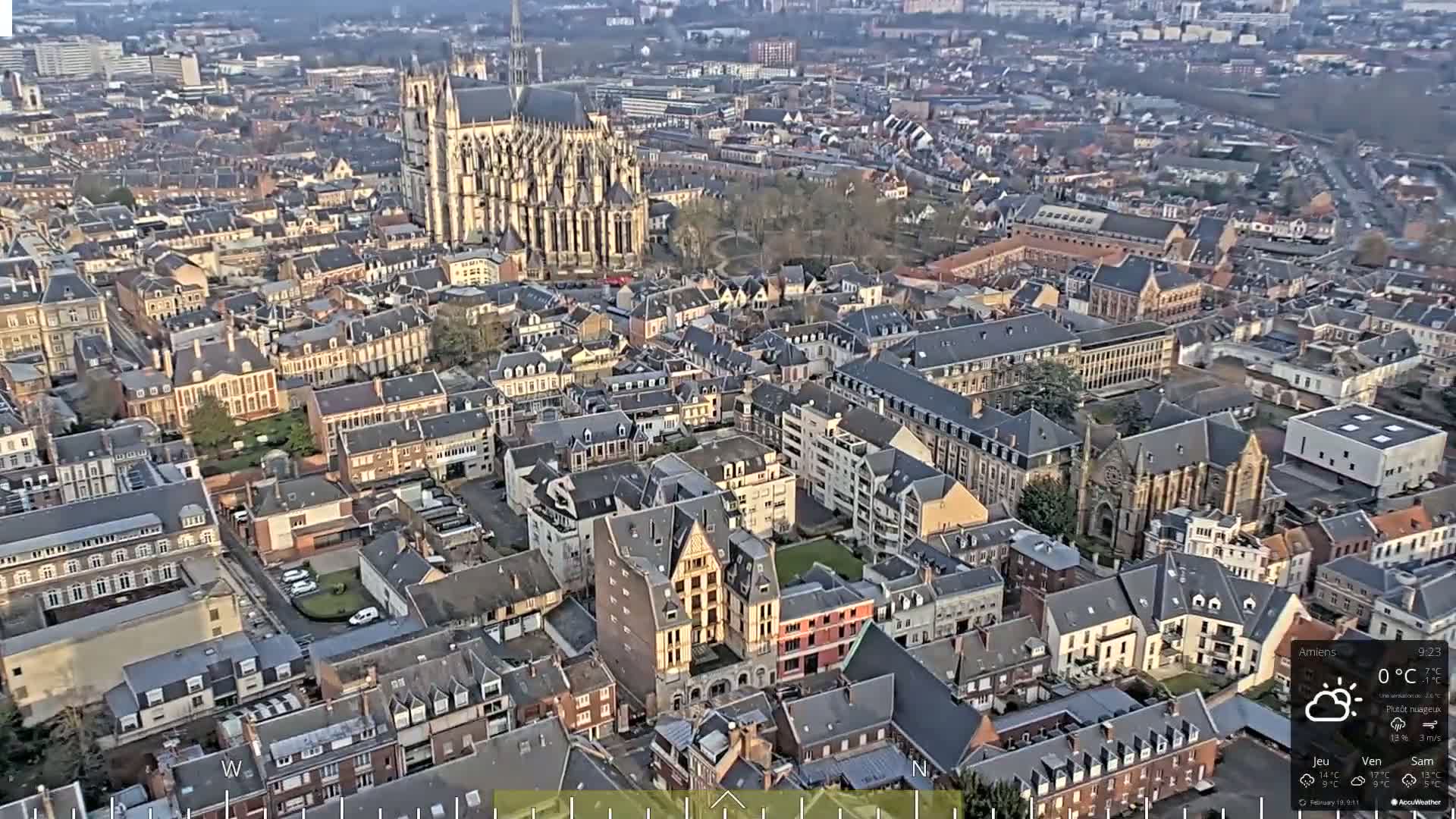 An aerial view of a European city on a partly cloudy day, showing a large cathedral and numerous closely packed buildings.