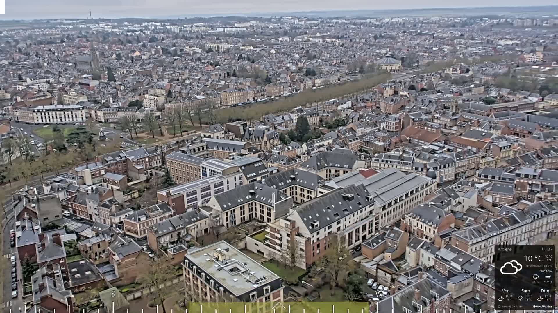 An aerial view of a densely populated city on an overcast day shows numerous buildings with dark gray roofs.