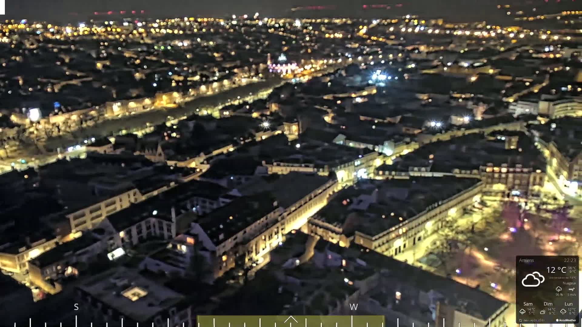A nighttime aerial view of a city with many illuminated buildings and streets under cloudy skies.