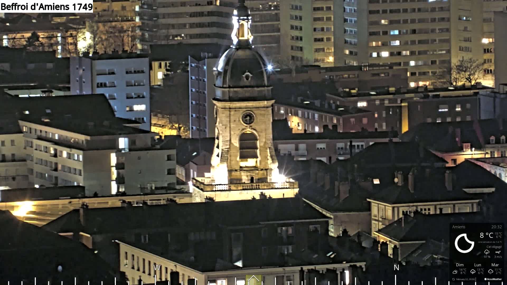 A brightly lit clock tower stands prominently amidst a cityscape at night under clear skies.