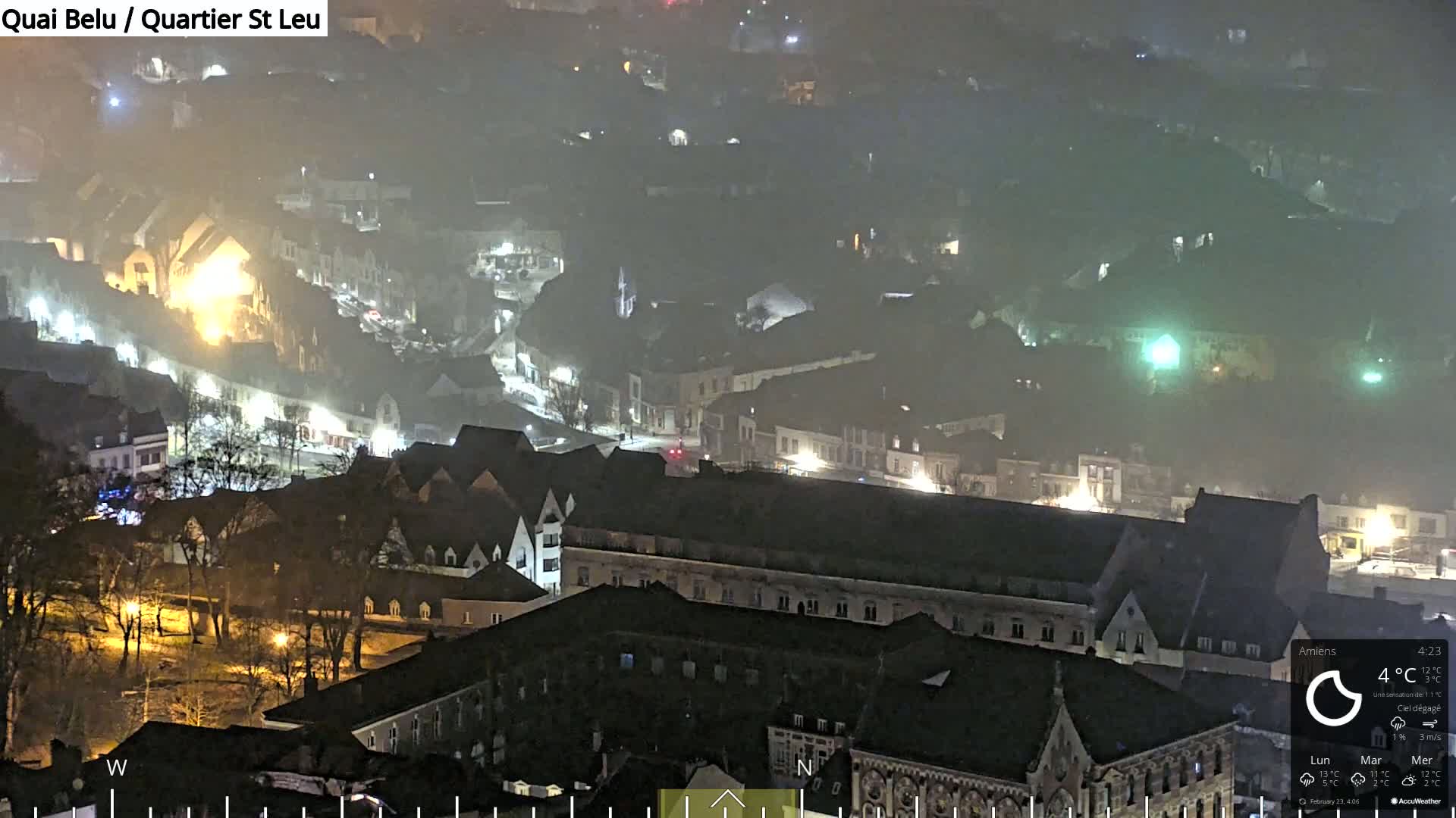 A nighttime, hazy view of a town with numerous buildings illuminated by streetlights.