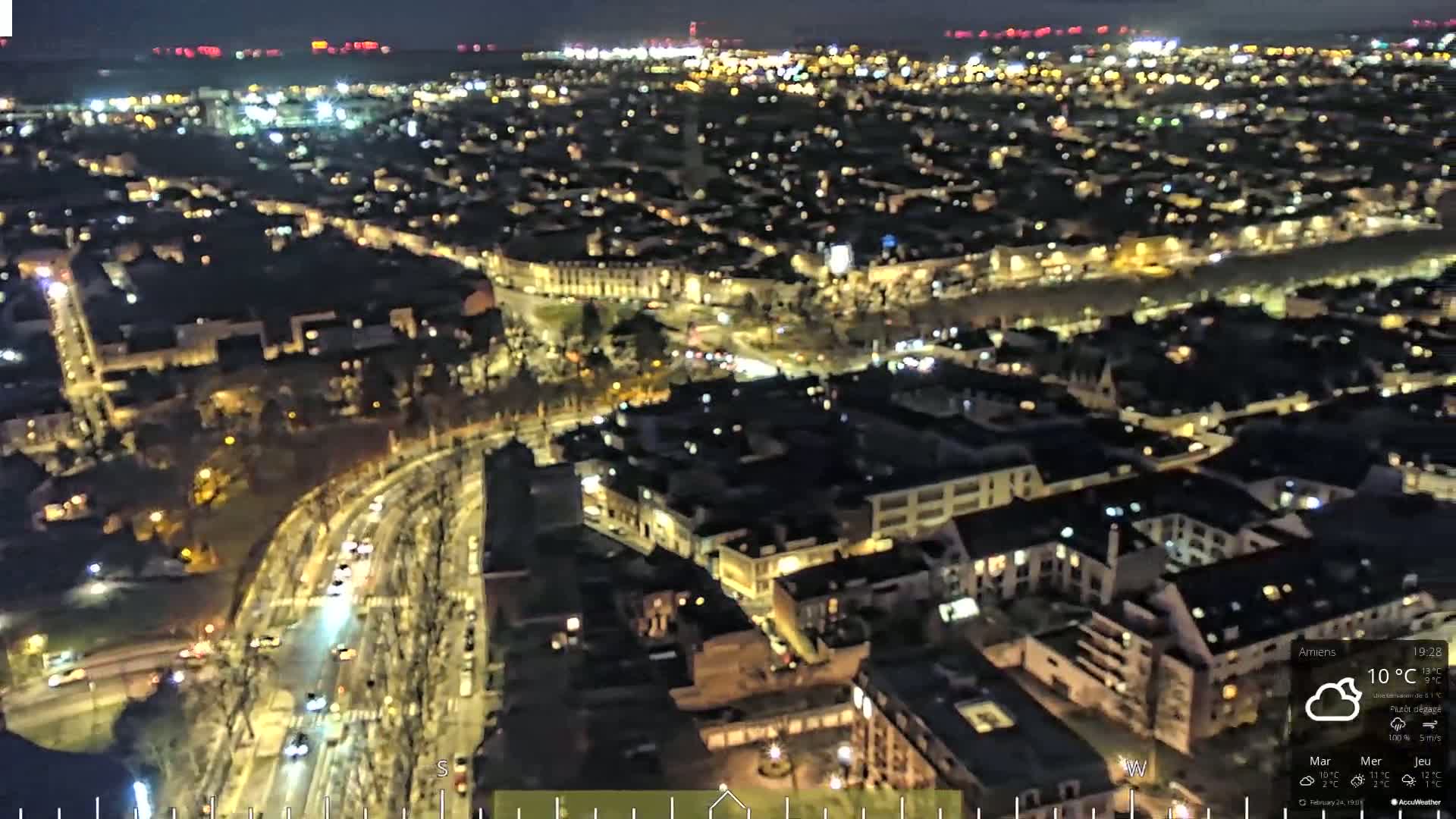A nighttime aerial view of a city with illuminated buildings and streets, under a mostly clear sky.