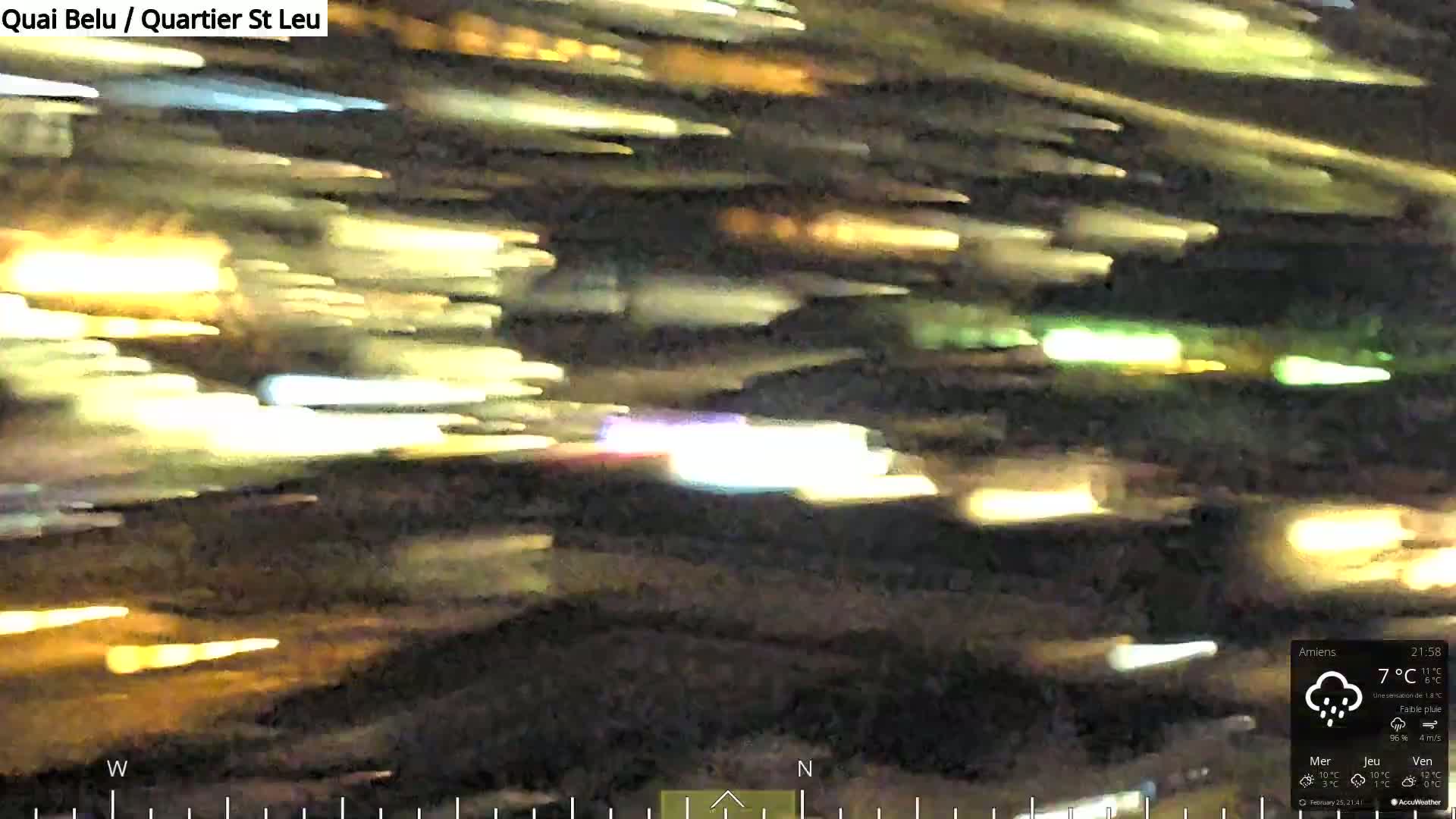 A blurry, nighttime image shows streaks of light from moving vehicles under a light rain.