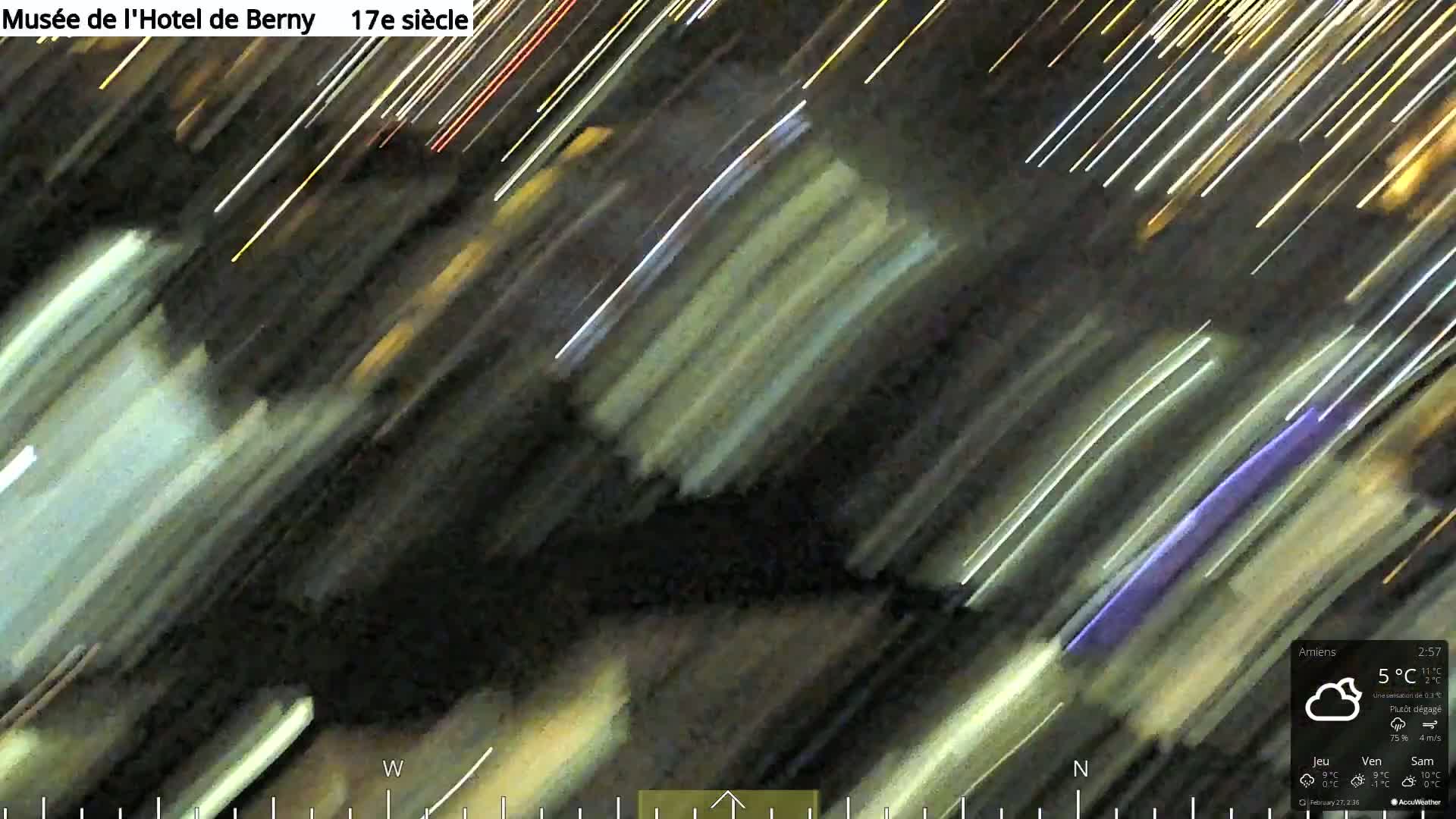 A blurry, time-lapse image shows streaks of light against a dark background at night under partly clear skies.