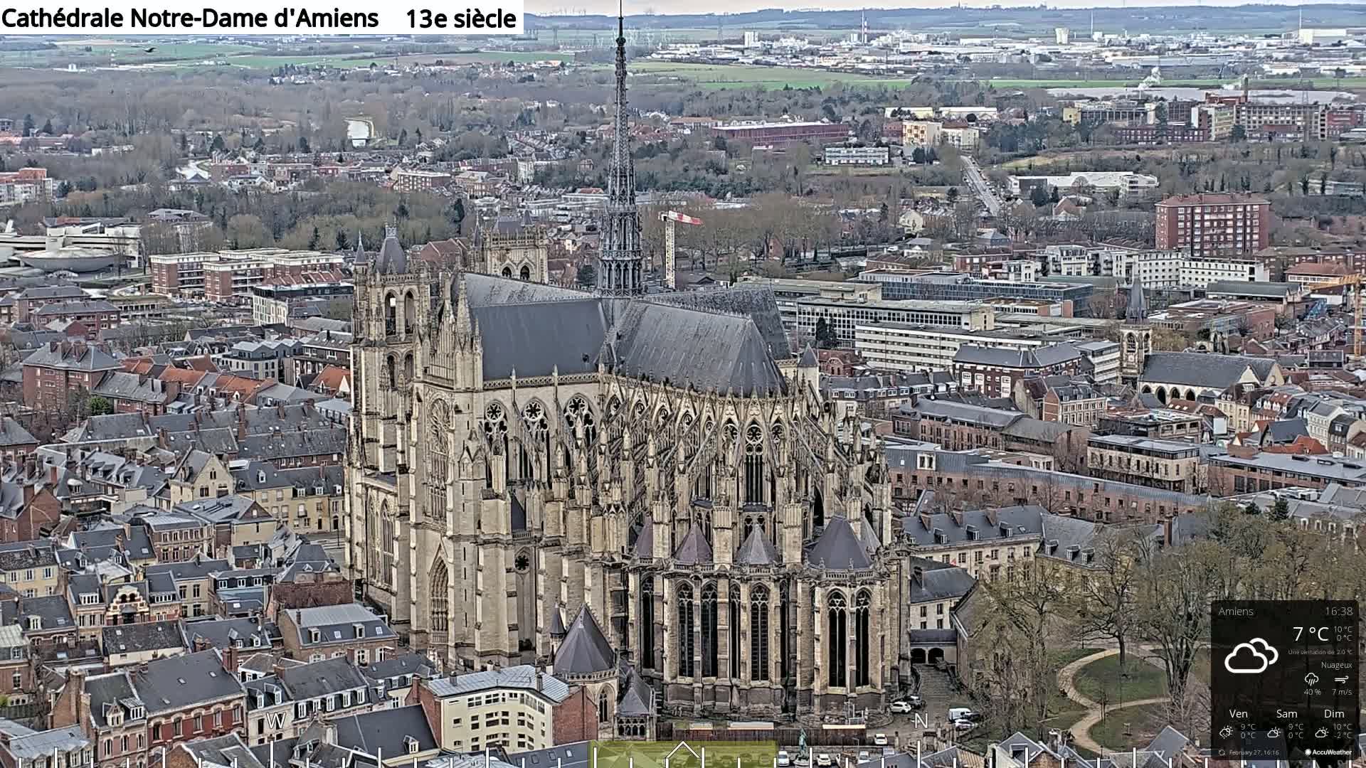 A large, ornate Gothic cathedral sits amidst a city of closely packed buildings on a cloudy day.