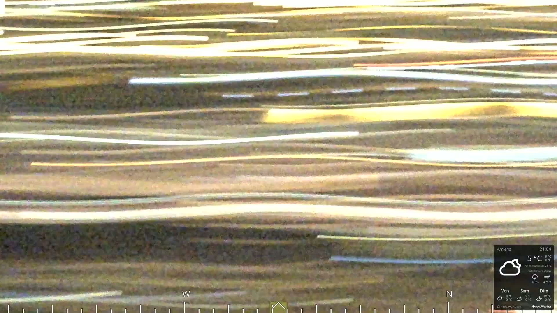 Streaks of light, likely from cars, create a horizontally layered pattern against a dark background under partly cloudy conditions.
