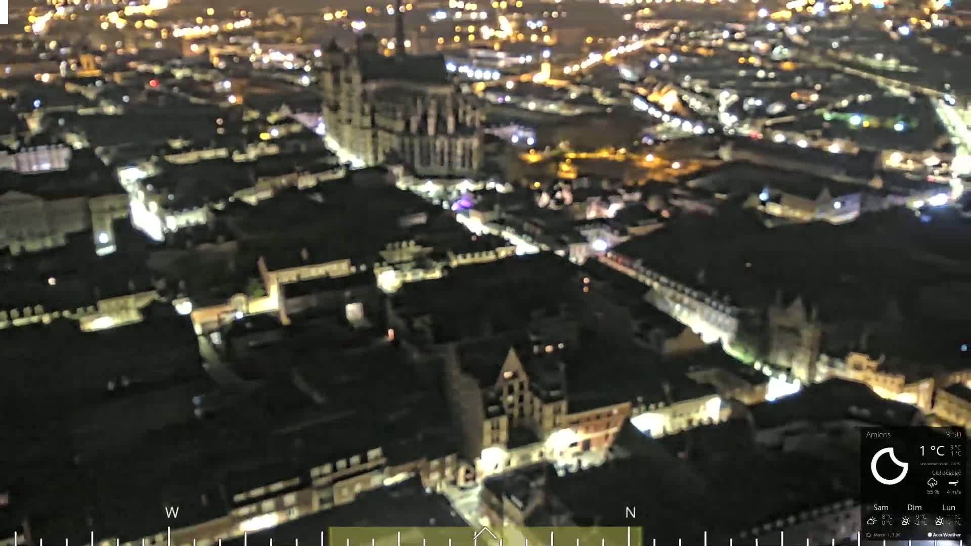 A nighttime aerial view of a city with illuminated buildings and streets, under clear skies.