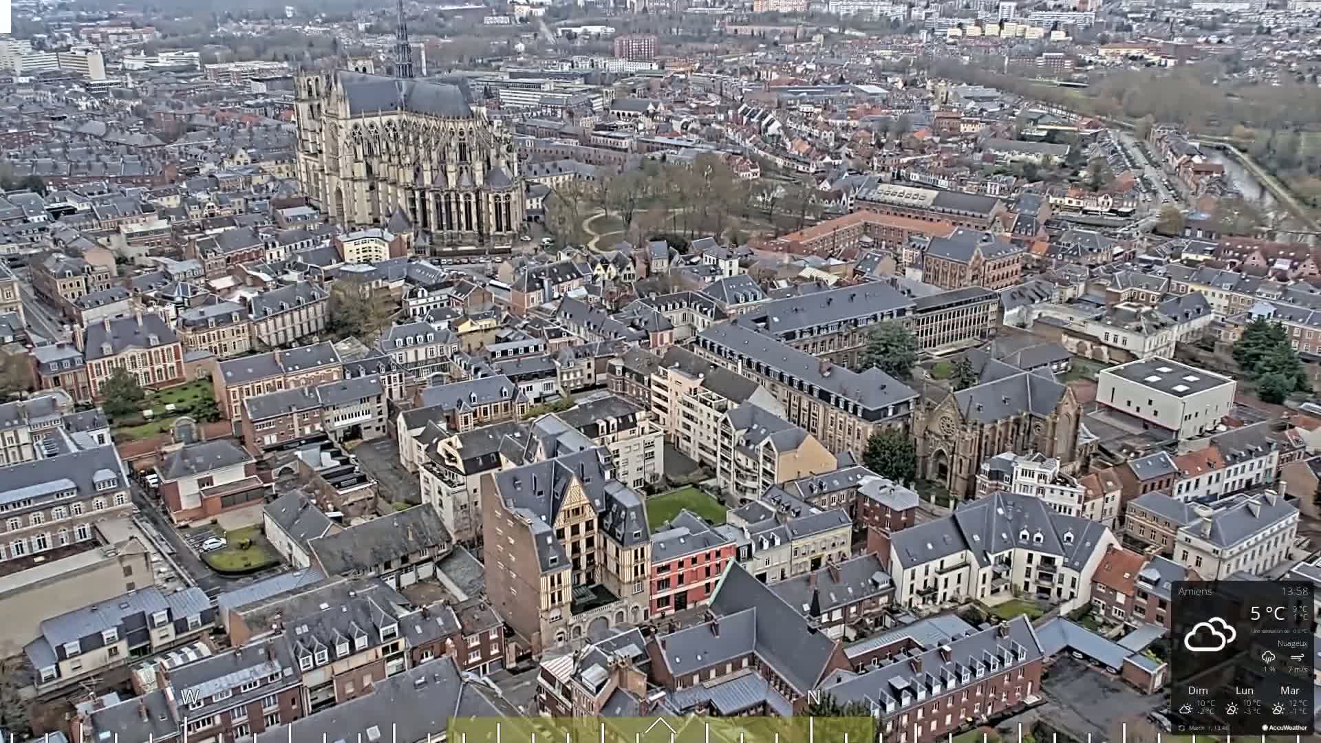 An aerial view shows a European city on a cloudy day, with a large cathedral prominently featured.