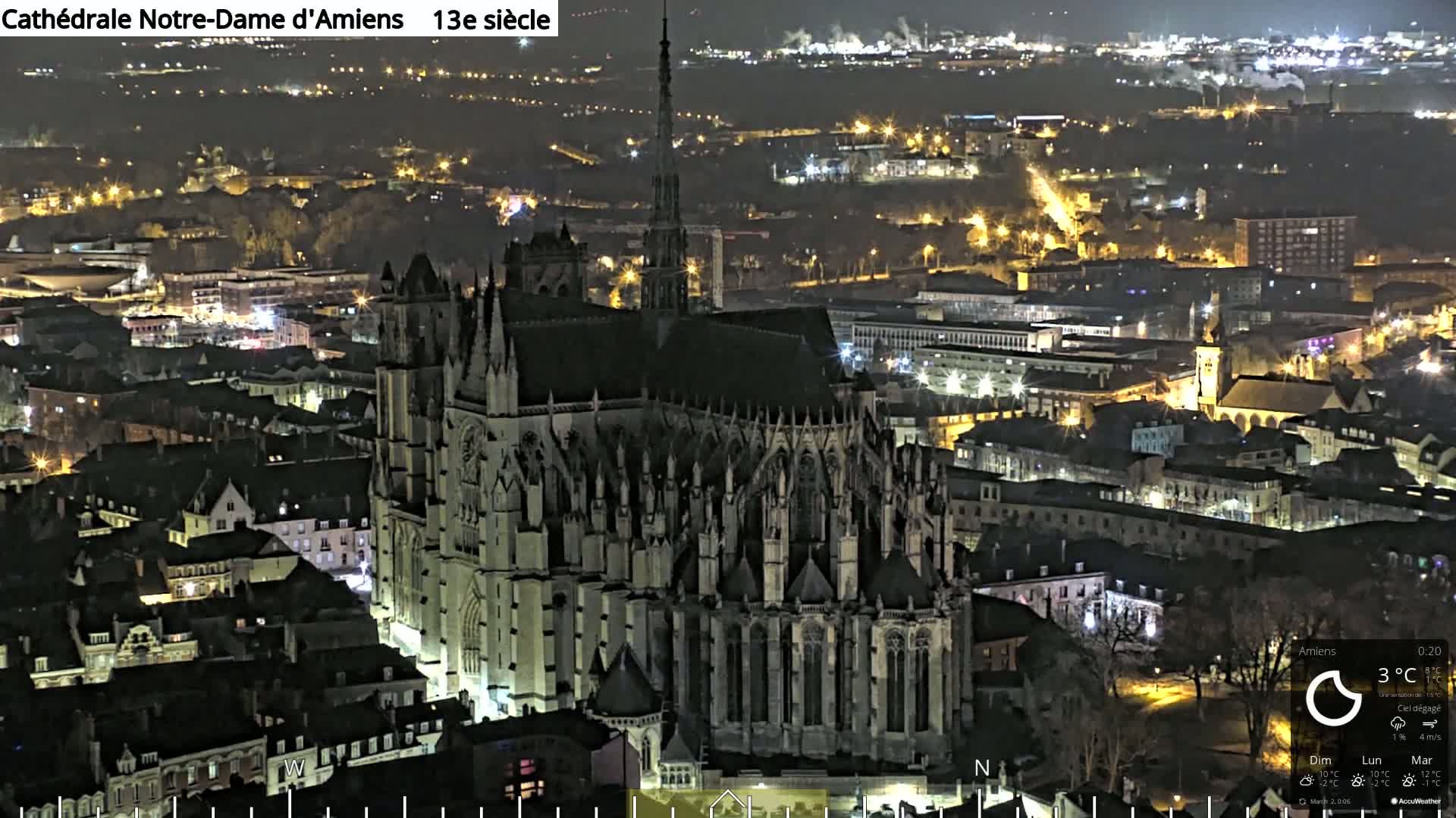 A large Gothic cathedral is illuminated at night, overlooking a city with many lights.