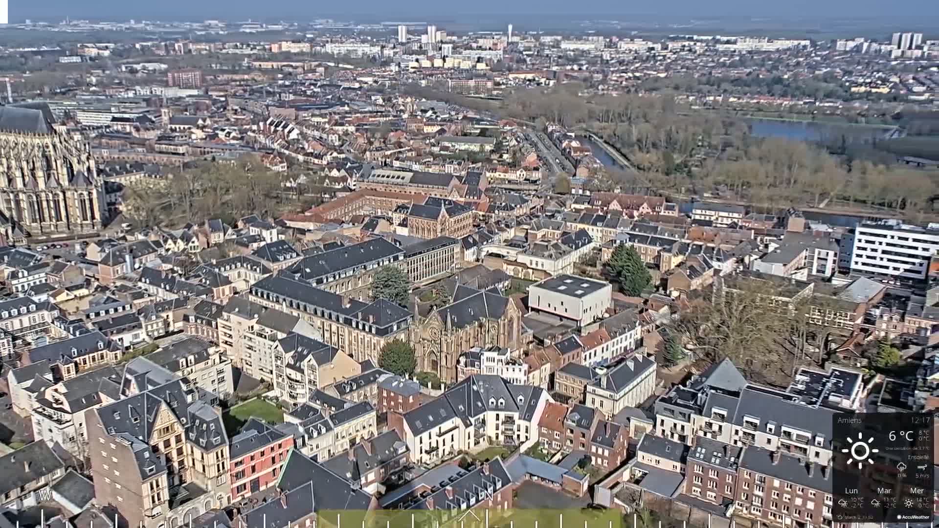 An aerial view of a European city on a sunny day shows a large cathedral and numerous closely packed buildings.