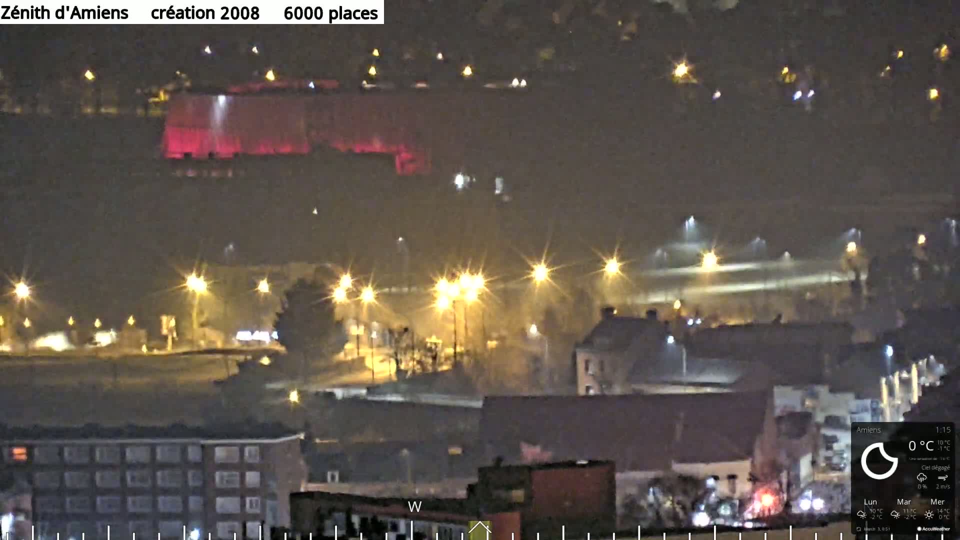 A nighttime aerial view of a city with a large red-lit building in the distance under a clear sky.