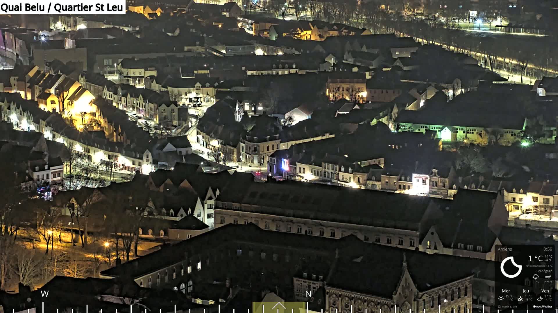 A nighttime aerial view of a European town with many buildings illuminated, under clear skies.
