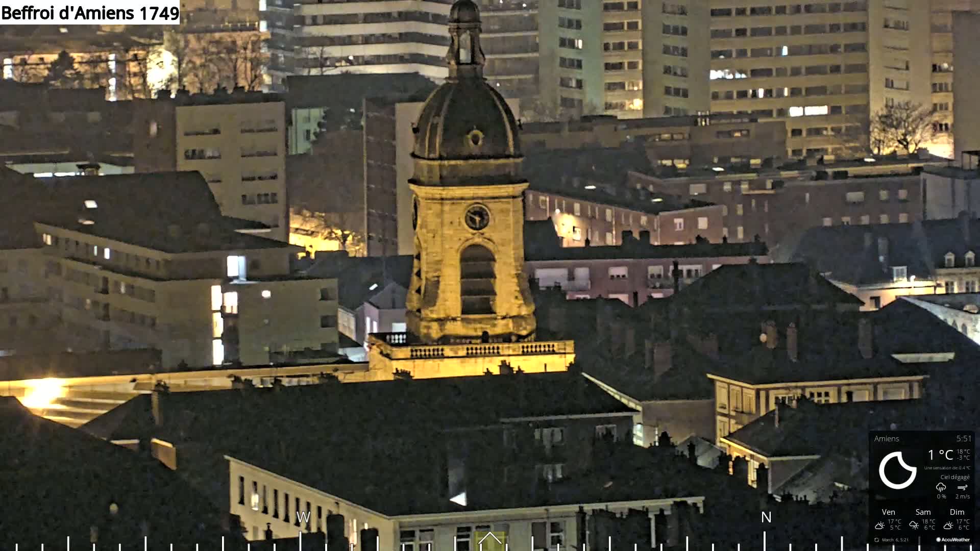 A nighttime aerial view of a city with a prominent, illuminated clock tower, under clear skies.