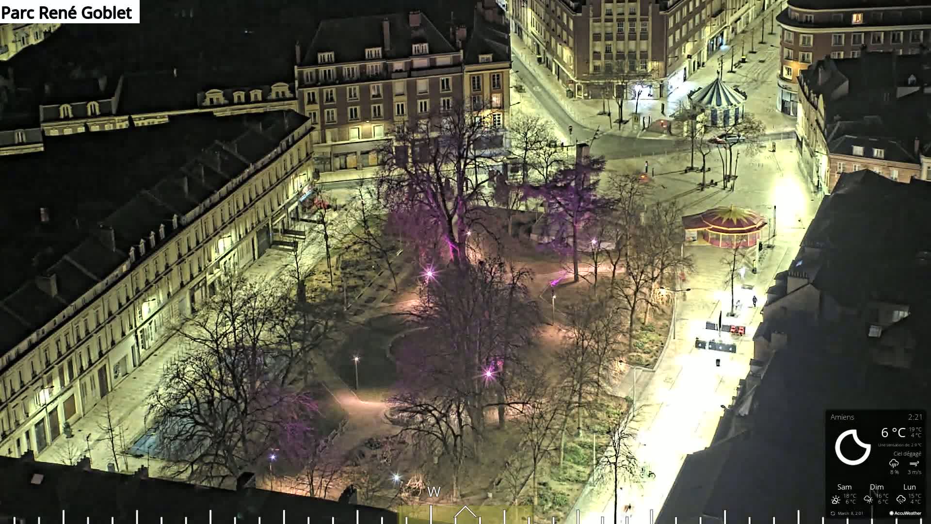 An aerial nighttime view of a park surrounded by buildings, illuminated by streetlights under a clear sky.