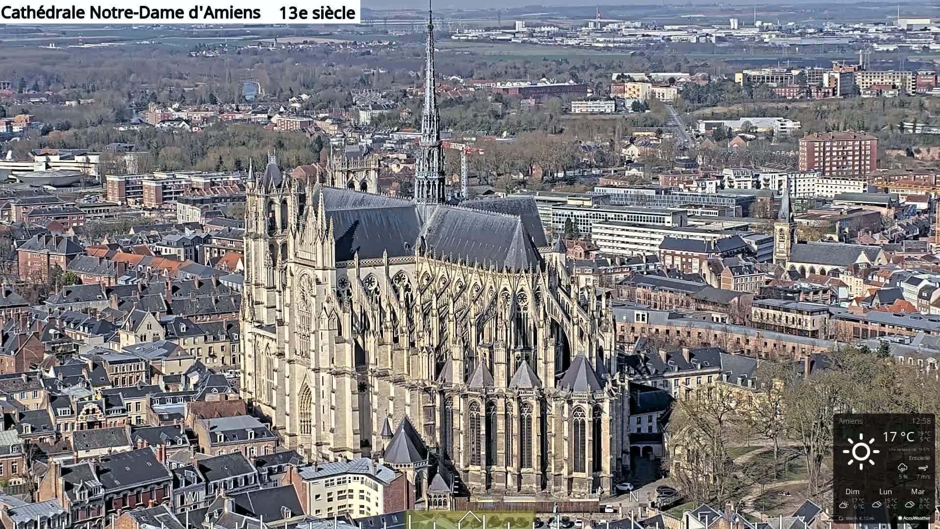 A large Gothic cathedral stands prominently in a densely populated city on a sunny day.