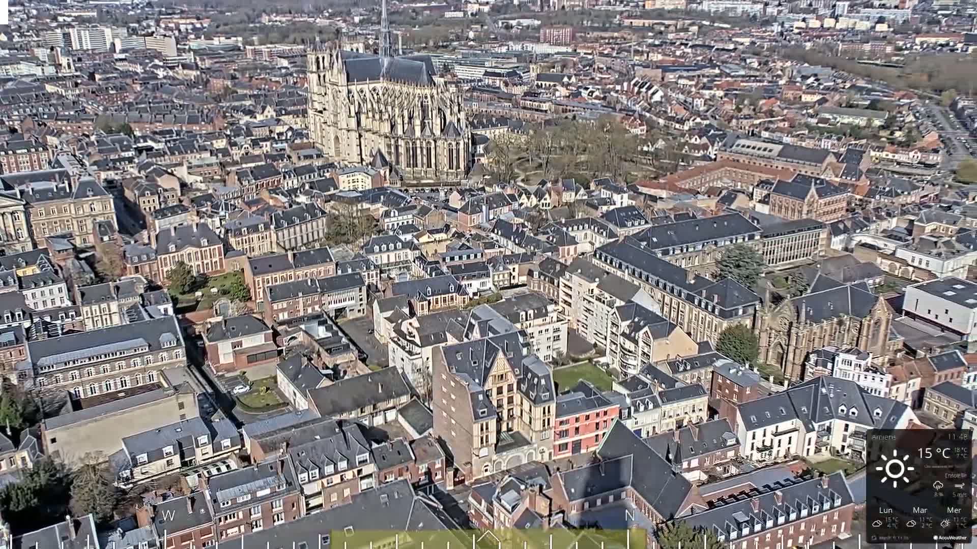 An aerial view of a European city on a sunny day shows a large cathedral and many closely-packed buildings of similar style and size.