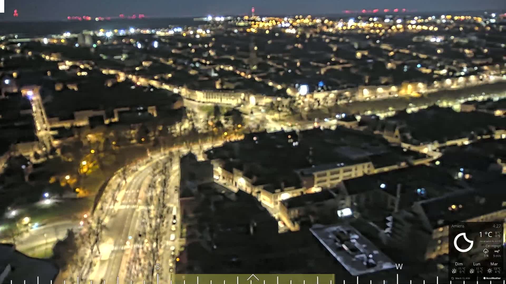 A nighttime aerial view of a city with many illuminated buildings and streets, under a clear sky.