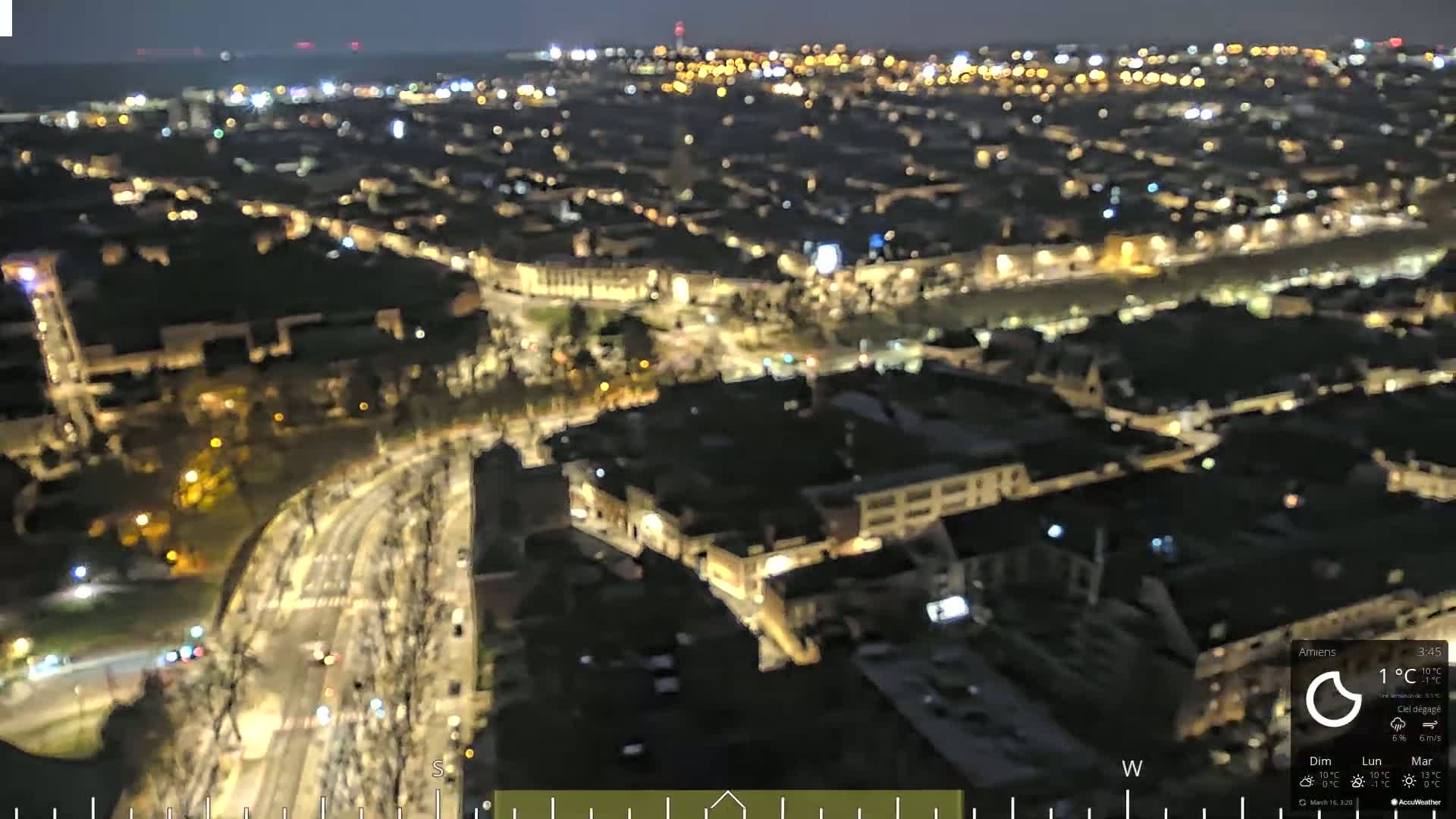 A nighttime aerial view of a city illuminated by streetlights and building lights under a clear sky.