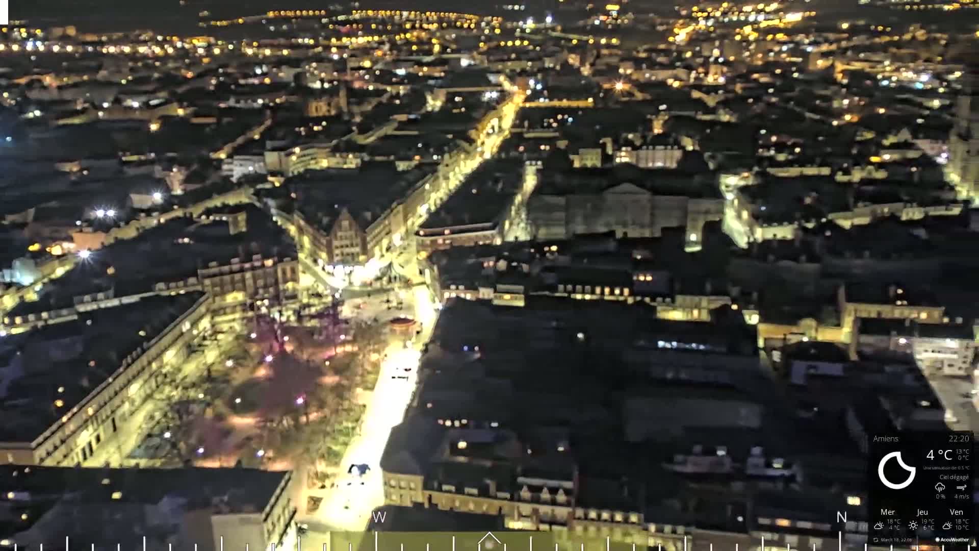 A nighttime aerial view of a city with brightly lit streets and buildings, under clear skies.