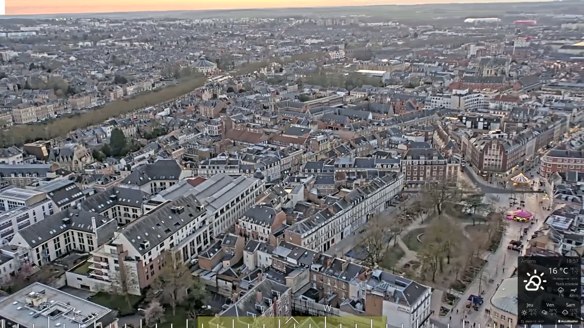 An aerial view shows a city with many closely packed buildings under partly sunny skies.