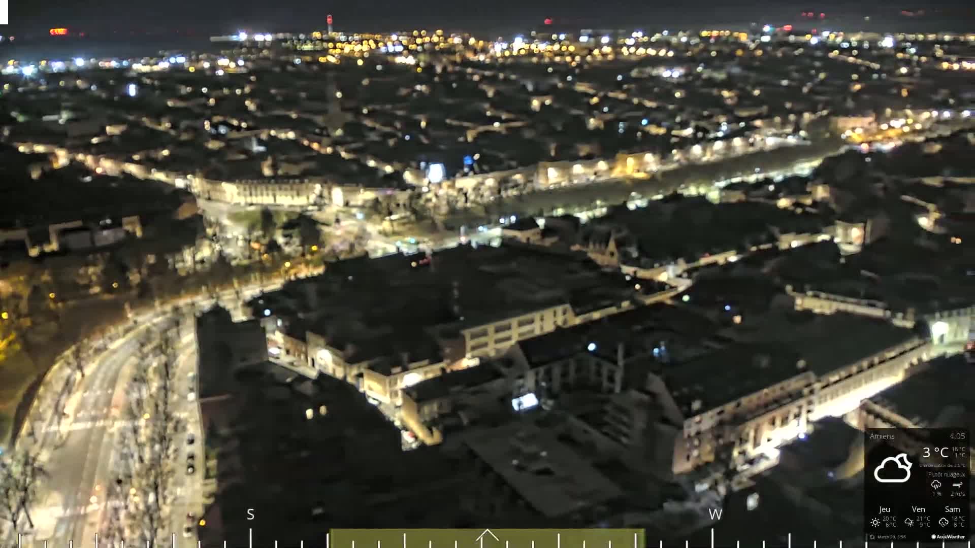 A nighttime aerial view of a city with dimly lit buildings and streets, under partly cloudy skies.