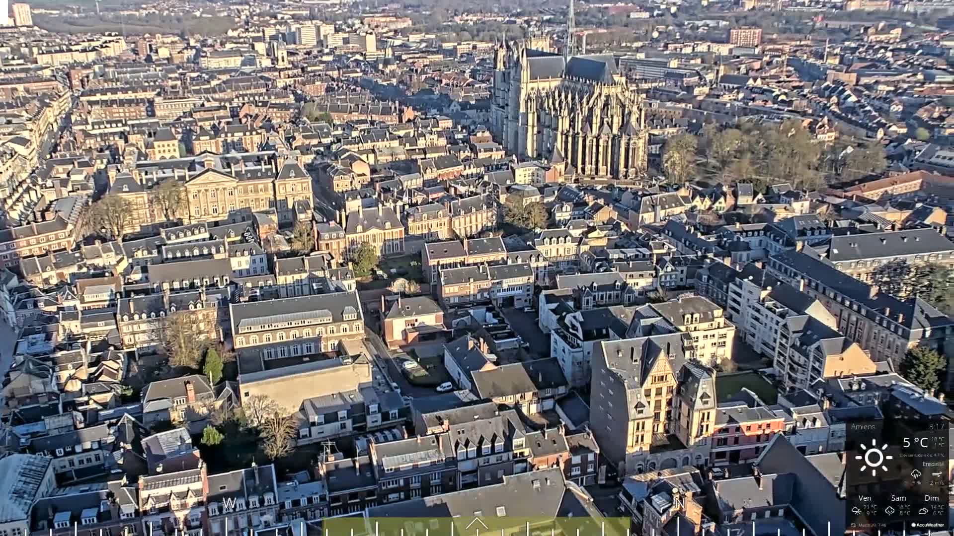 An aerial view of a densely populated city with a large cathedral in the background on a sunny day with a temperature of 5°C.