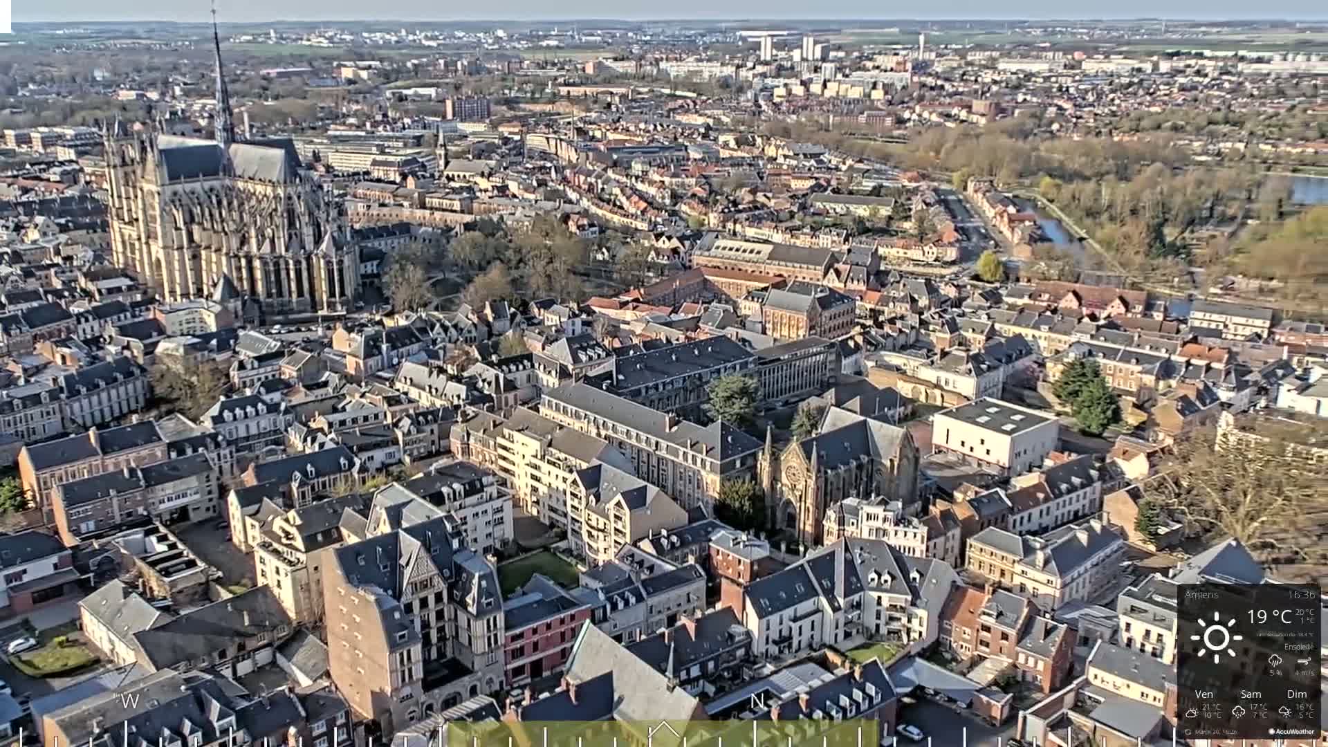 An aerial view of a European city on a sunny day, showing a large cathedral and numerous closely packed buildings.