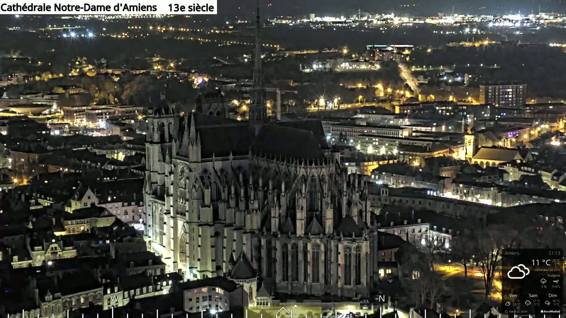 A large Gothic cathedral is illuminated at night, surrounded by a city with many other lights.