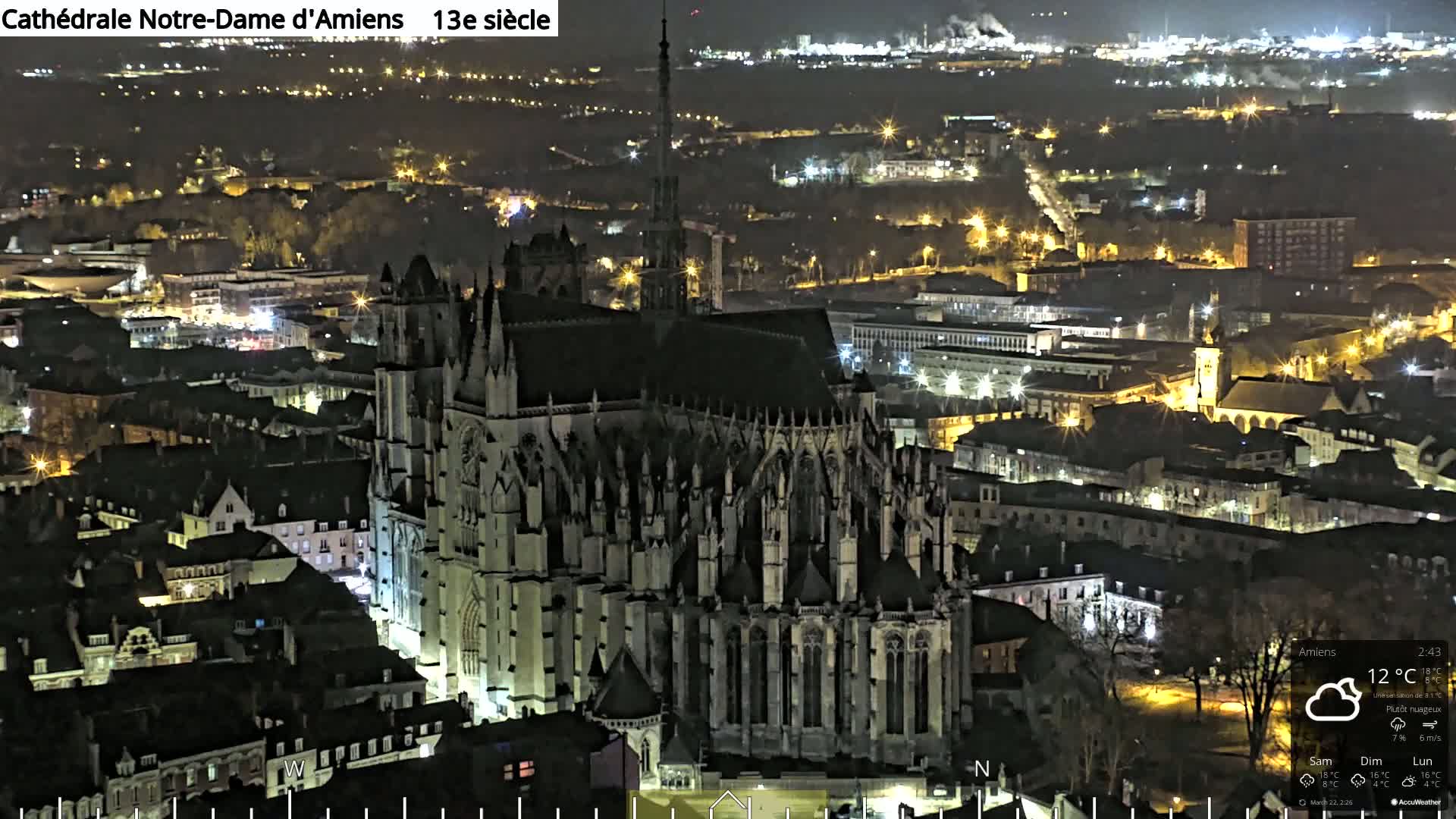 A large Gothic cathedral is illuminated at night, overlooking a city with numerous lights.