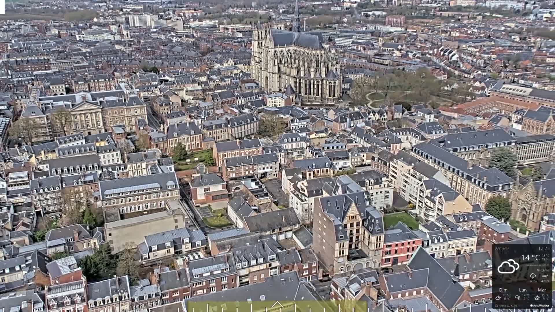 An aerial view of a European city on a partly cloudy day, showing a large cathedral and densely packed buildings of varying heights and architectural styles.