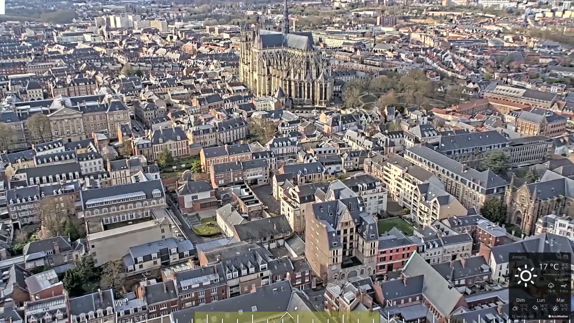 Here is a description of the image: An aerial view of a European city on a partly sunny day shows a large cathedral and many closely-packed buildings of various sizes and styles.