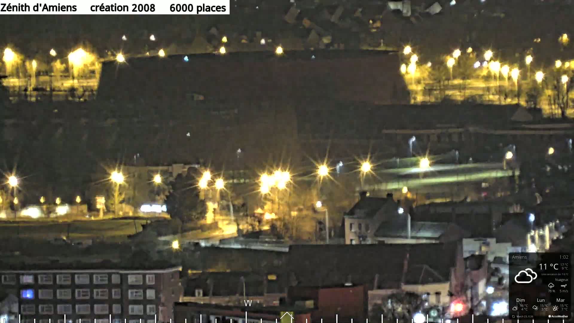 A nighttime aerial view of a city with numerous illuminated buildings and streetlights under cloudy skies.