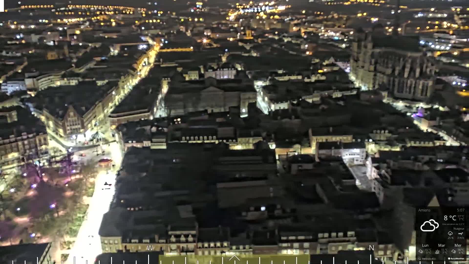 A nighttime aerial view of a city with cloudy weather shows many illuminated buildings and streets.