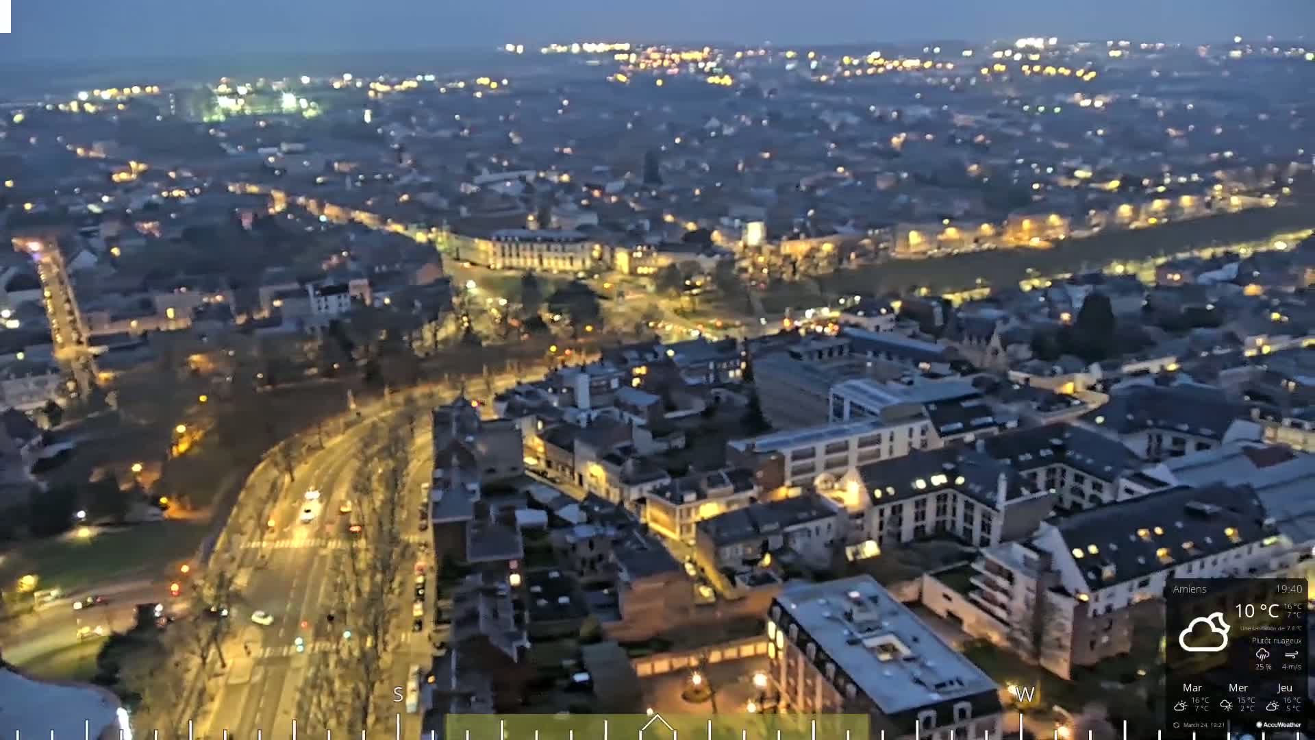 A nighttime aerial view of a city with many illuminated buildings and streets under partly cloudy skies.