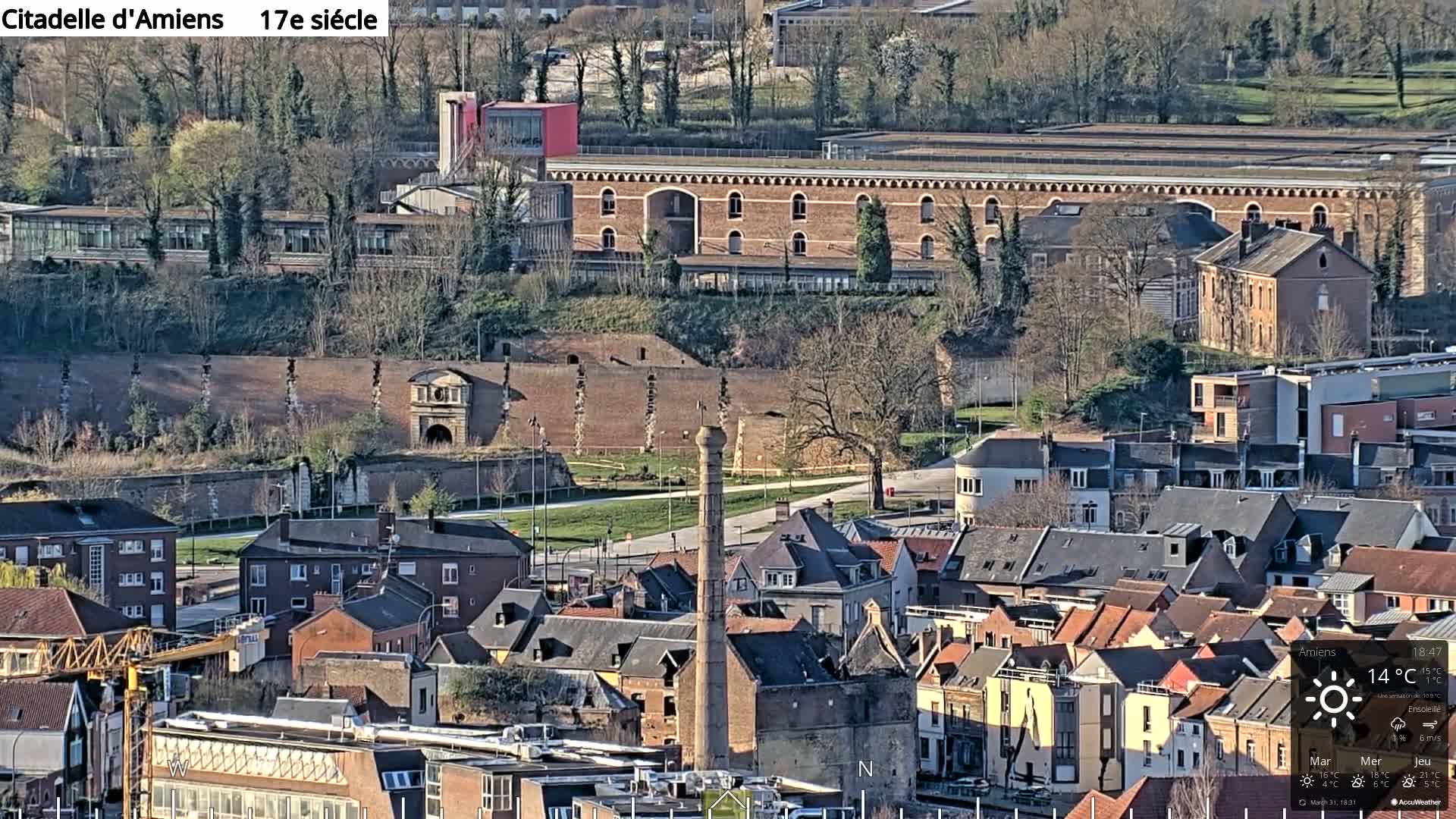 A high-angle, long shot of a town on a sunny day, featuring a brick citadel and many residential buildings.