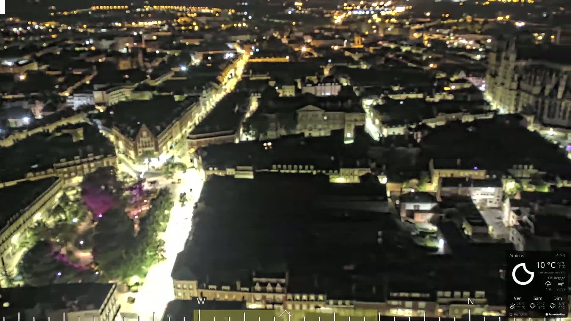 An aerial nighttime view of a city with brightly lit streets and buildings under clear skies.