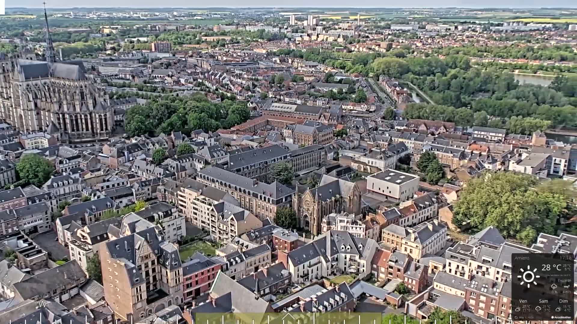 An aerial view shows a European city on a sunny day, featuring a large cathedral and numerous closely packed buildings.