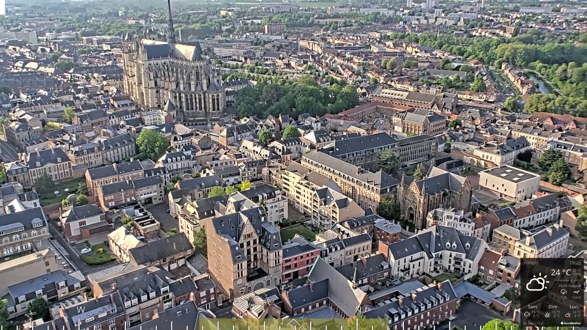 An aerial view of a European city on a partly cloudy day shows a large cathedral and many other buildings.