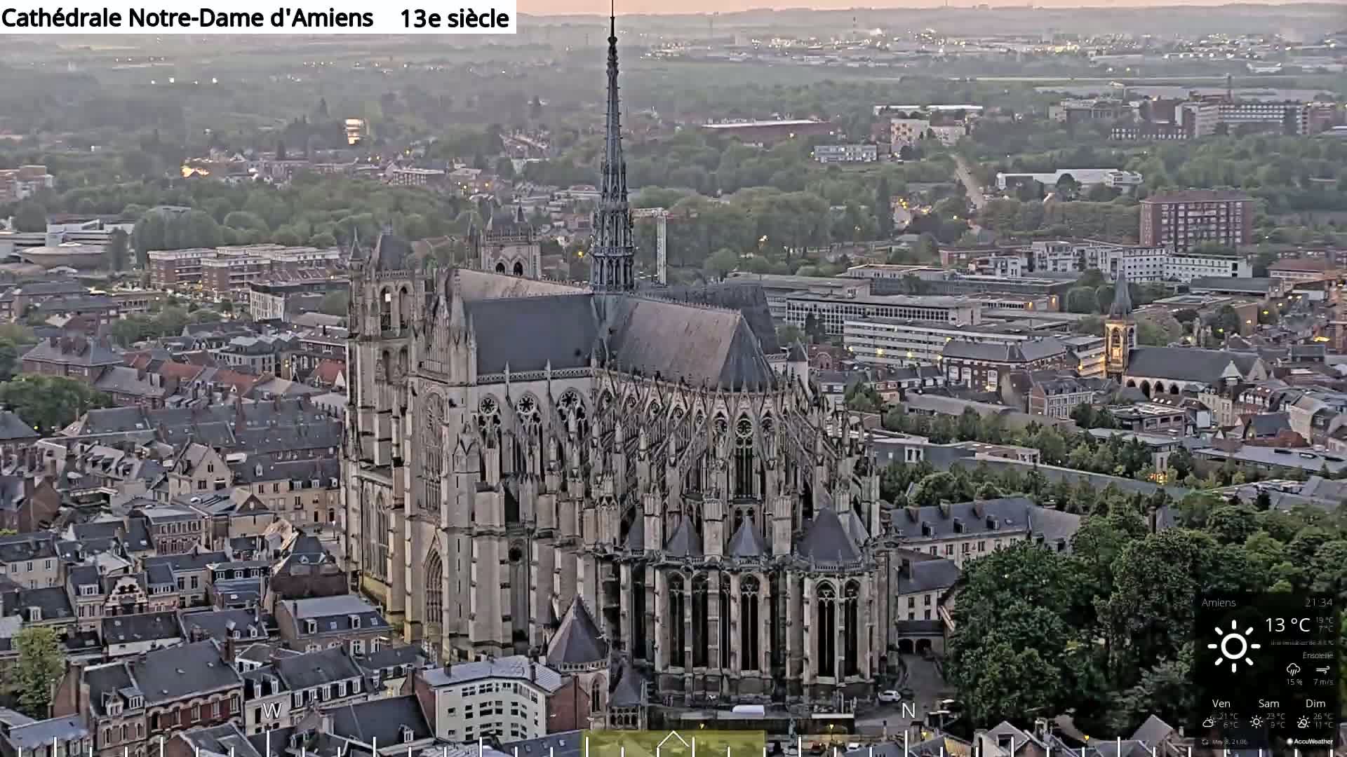 A large Gothic cathedral sits in the center of a city, viewed from above at dusk.